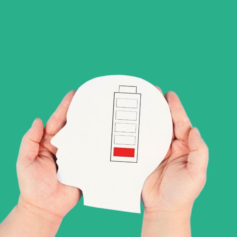 Hands holding a paper cutout of a human head with a low battery icon inside.